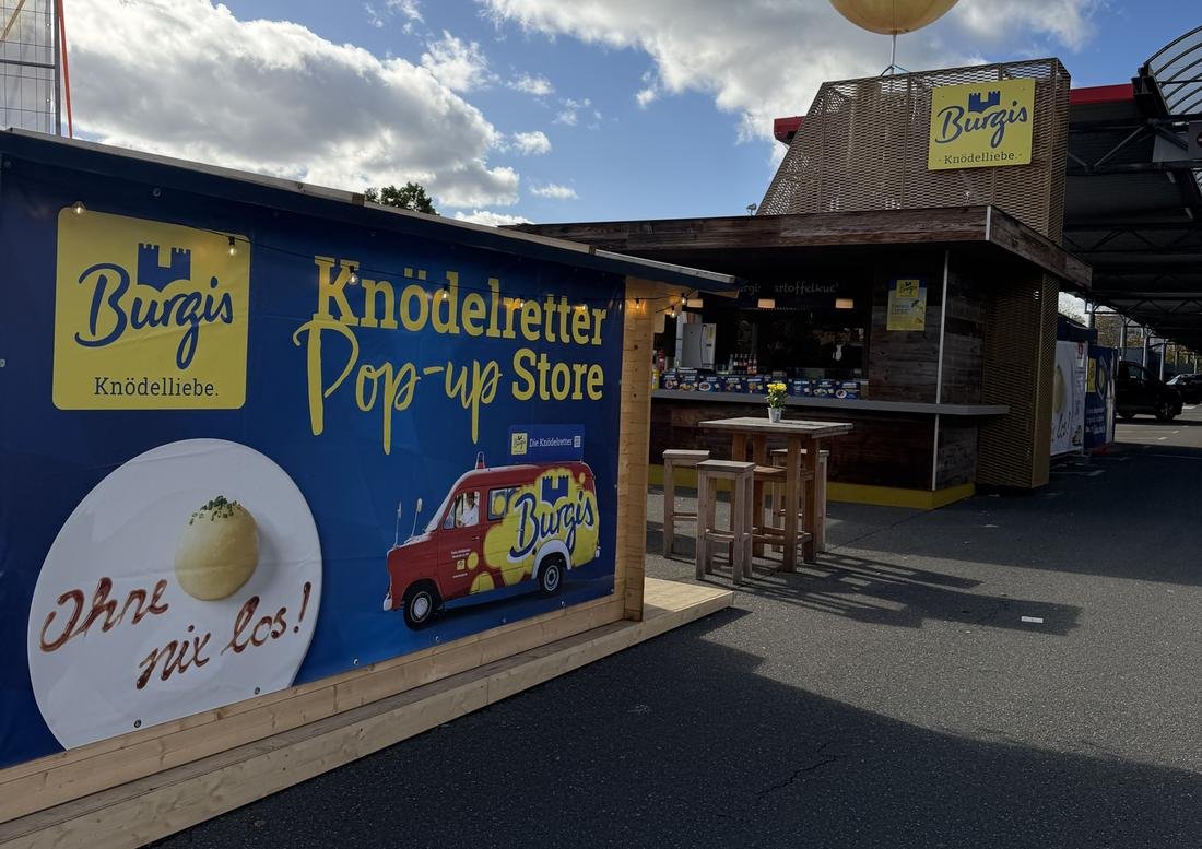 Der Knödelretter-Pop-up-Store mit Burgis-Banner und Imbiss-Hütte auf dem Selgros-Parkplatz